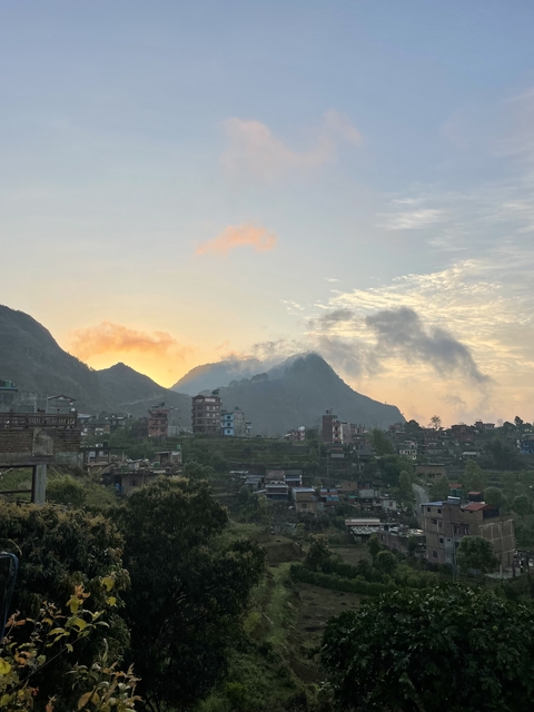 Sunset behind mountains and buildings with clouds in the sky.