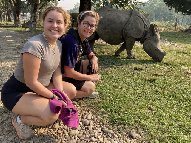 Two women sitting close to a grazing rhino.