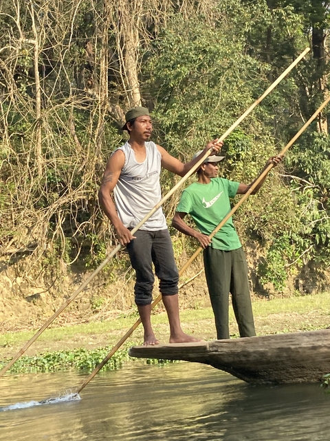       Two men paddling in shallow water with grass beside.
  