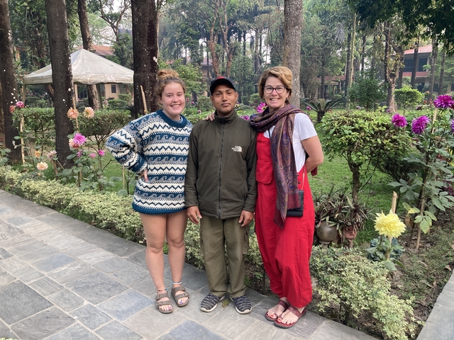       Three people posing in a garden with blooming flowers.
  