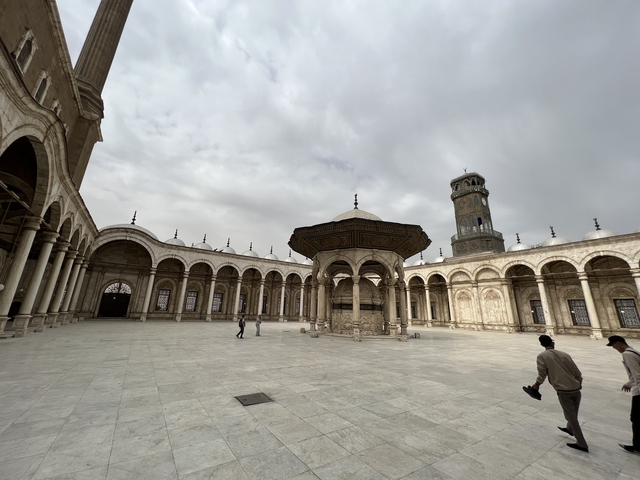       People walking in the courtyard of a mosque.
  