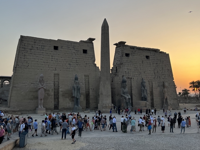       Large ancient temple entrance with an obelisk and many tourists.
  