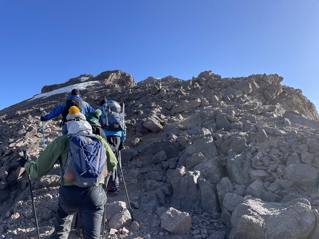 Hikers ascending a rocky mountain trail in sunlight.