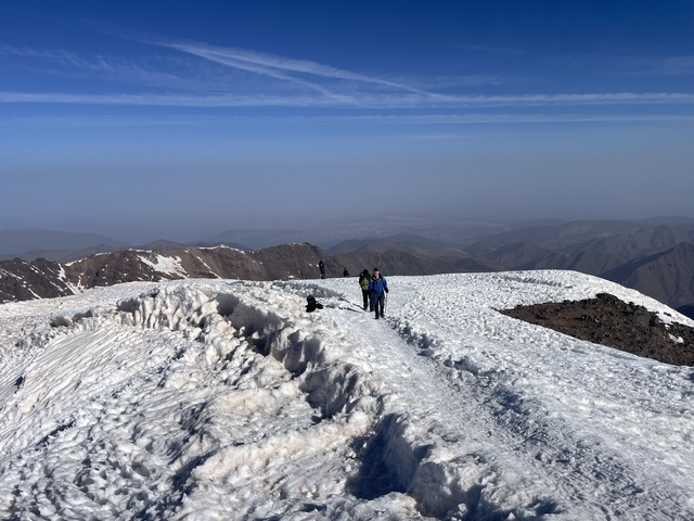 Hikers walking on a snow-covered mountain ridge with a view.