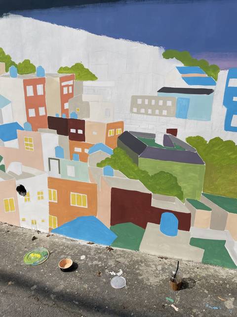       Unfinished mural painting on a wall with paint cans.
  