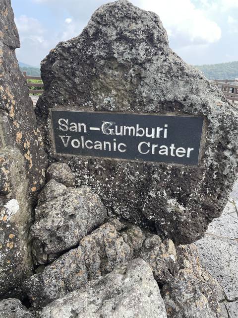 Rock formation with text "San-Gumburi Volcanic Crater."
