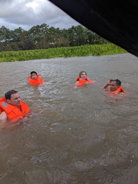       Group of people swimming in a body of water with life vests.
  