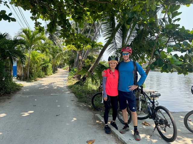       Two cyclists posing by a road lined with palm trees.
  