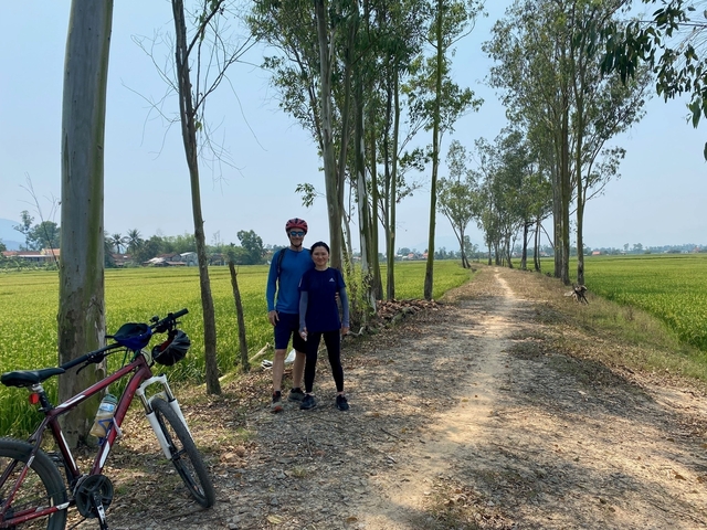       Two cyclists standing on a dirt path surrounded by trees.
  