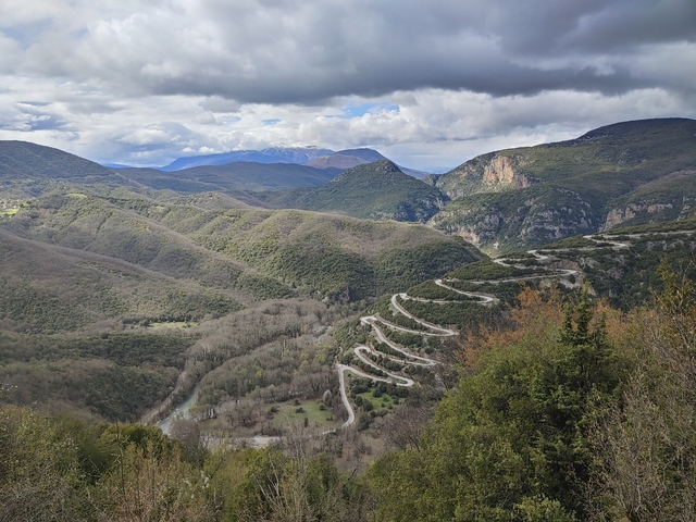       Winding road through a mountainous landscape with cloudy skies.
  