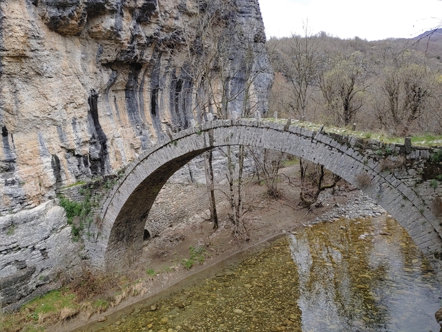 Stone arch bridge over a shallow river in a canyon.