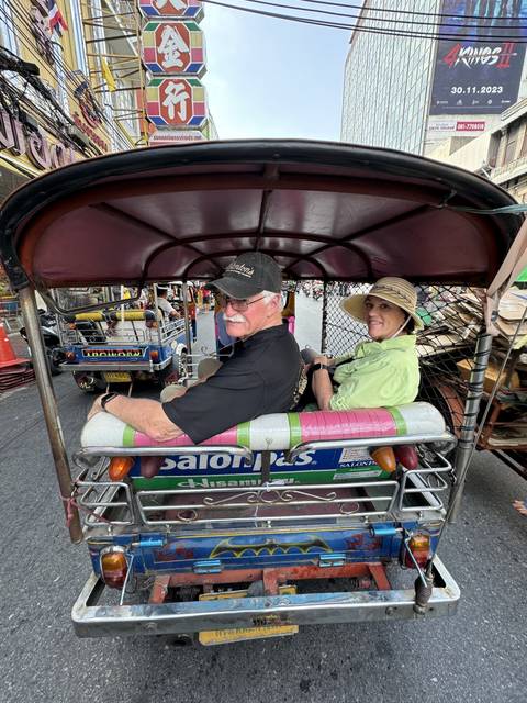 Tourists smiling on a tuk-tuk ride through a city.