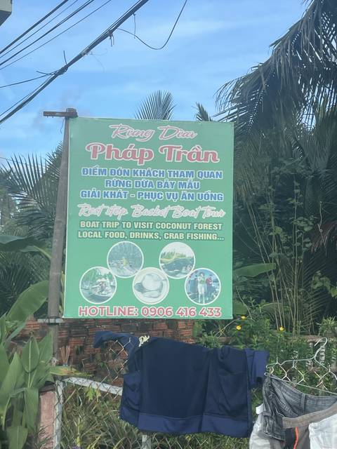 A roadside sign in Vietnamese language with a background of palm trees.