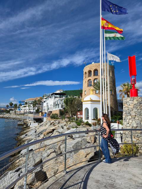       A person walking along a walkway with flags and a tower in the background.
  