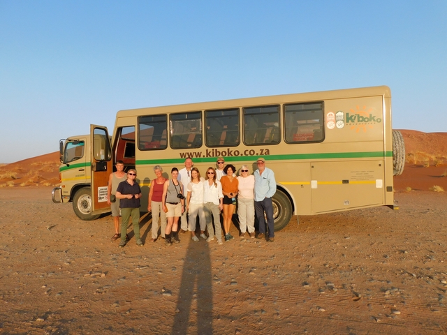 A group of people posing with a tour bus in a desert environment.