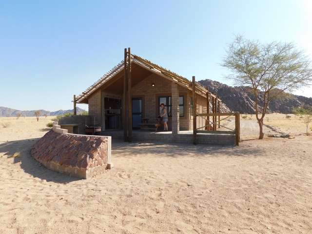 A small cabin in a desert landscape with a person standing at the entrance.