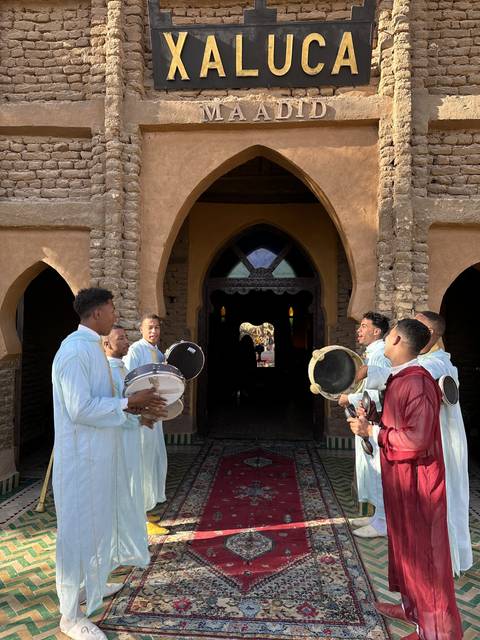       People in traditional attire with drums, standing in front of a building entrance.
  