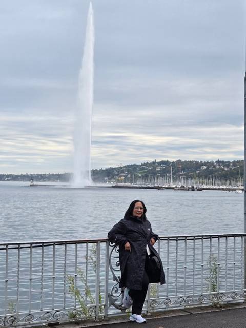       Person sitting by a lake with a tall water fountain.
  
