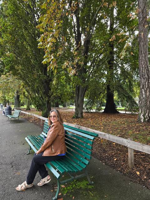      Person sitting on a bench in a park with autumn leaves.
  