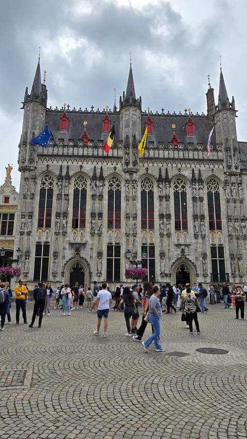 Large ornate building with flags and cobblestone square.
