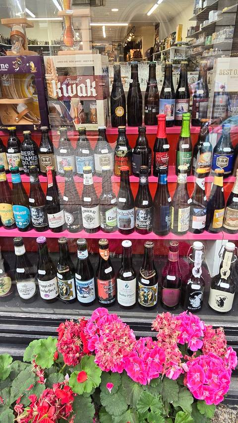       Bottles of beer displayed in a shop window with flowers.
  
