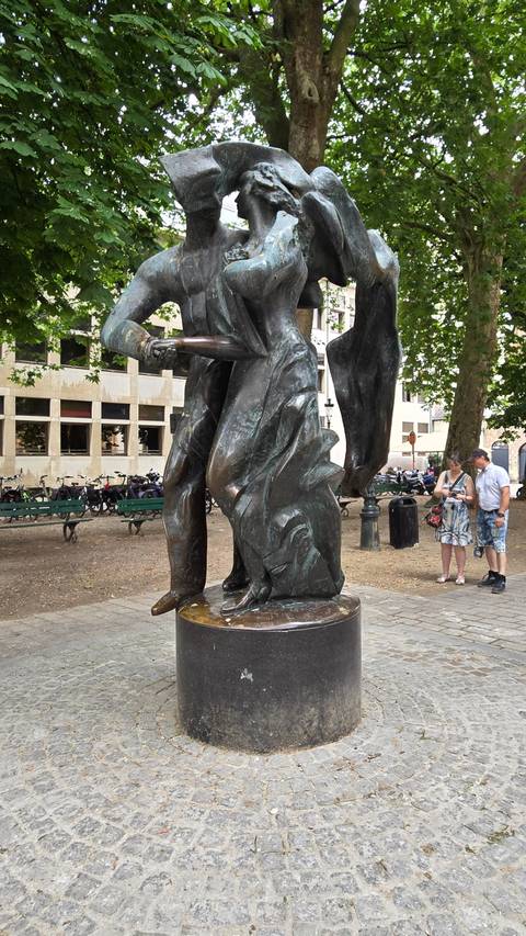       Bronze statue of a man in a flowing cloak on a cobblestone street.
  