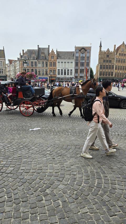       A horse-drawn carriage with people walking in a cobblestone square.
  