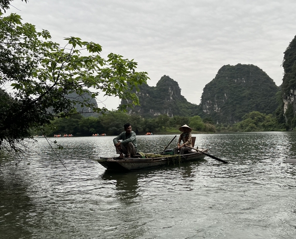       Two people in a traditional boat on a peaceful river.
  