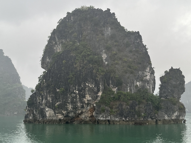 A tall rocky outcrop emerging from water, under a cloudy sky.