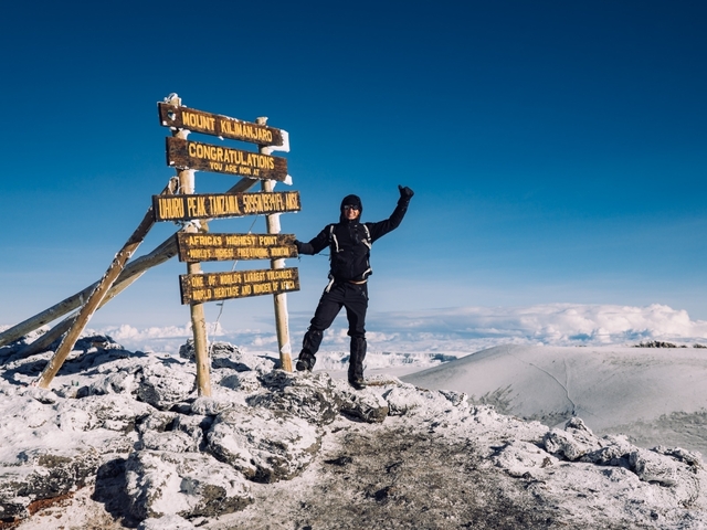 Individual celebrating at the snowy summit of Mount Kilimanjaro.