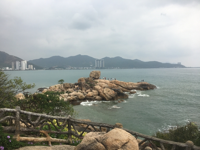 Coastline with rocks and sea, high-rise buildings in the distance.