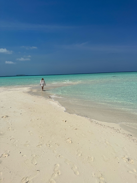 Woman walking on a pristine sandy beach with turquoise waters.