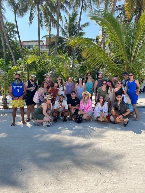 Group of people posing on a beach under palm trees.