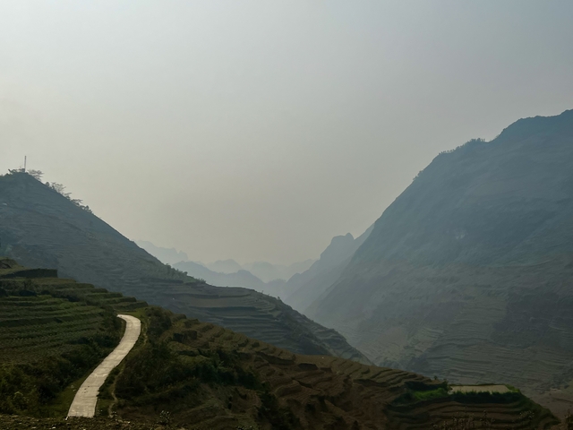       Terraced fields leading towards mountains with a hazy sky.
  