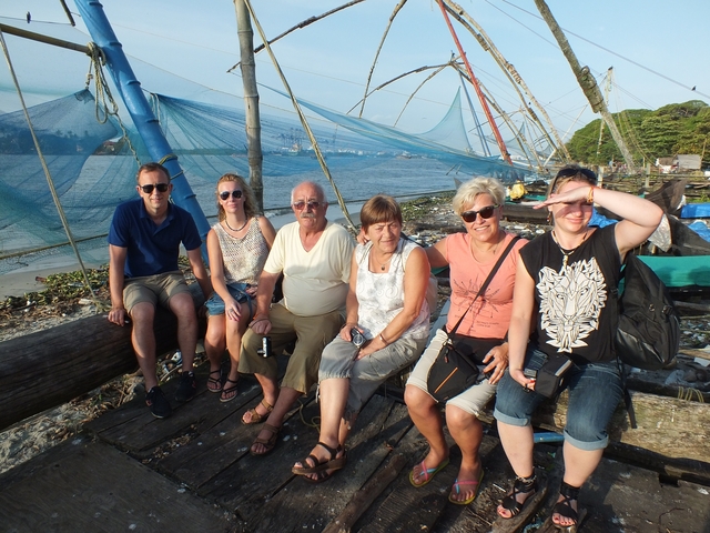 Group of people sitting by fishing nets and a riverbank.