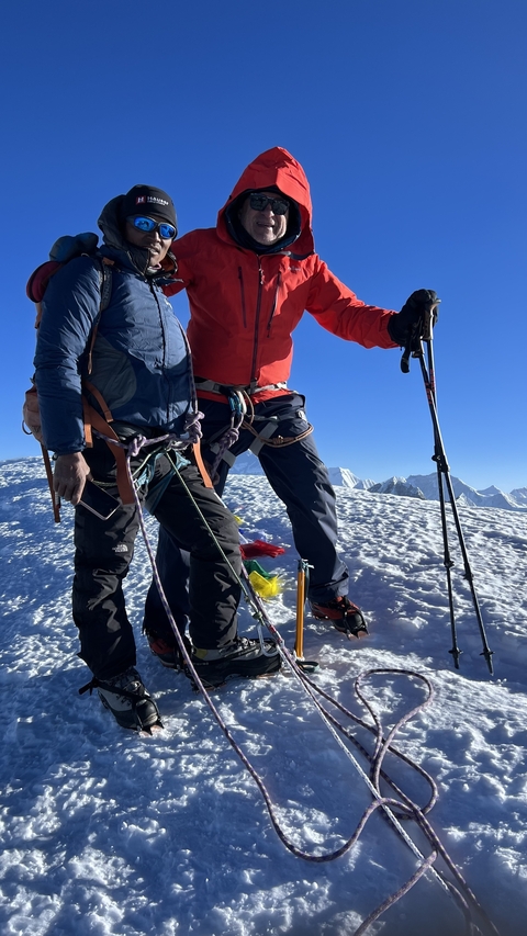       Two climbers standing on snow with mountains in the background.
  