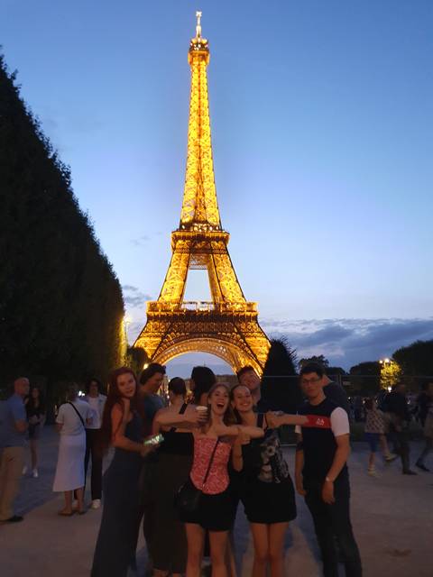Group of people posing with Eiffel Tower lit up at night.