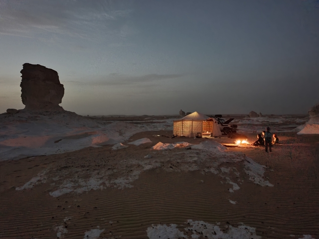 Campfire next to a tent in a desert at dusk.