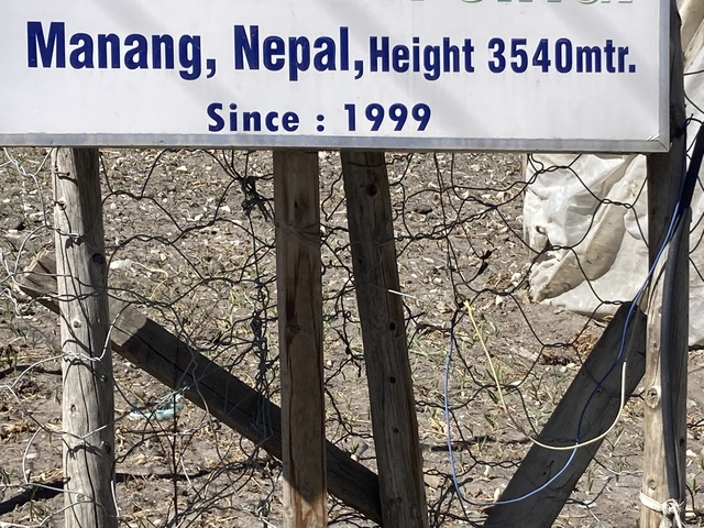 A close-up of a wooden sign with text and wire fencing.