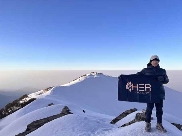       Person holding a flag on a snowy mountain peak with a clear blue sky.
  