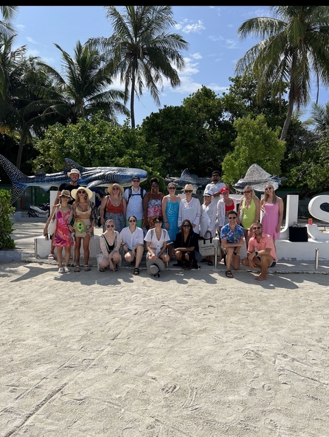 Large group of smiling people posing on the beach with marine life statues.