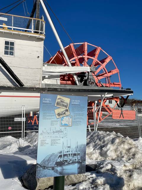       A large red wheel with an informational sign beside it in the snow.
  