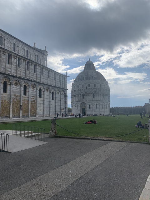A cathedral and baptistery with people in a green area