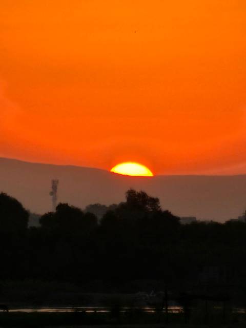       Sun setting behind hills with an orange sky.
  
