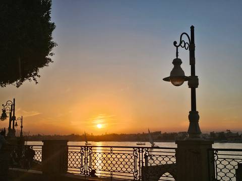       Sunset view over a river with silhouettes of cityscape and streetlights.
  