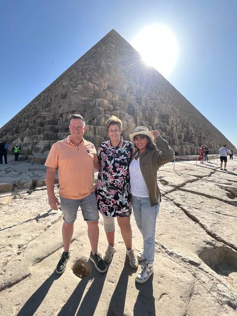       Three people posing with a pyramid in the background.
  