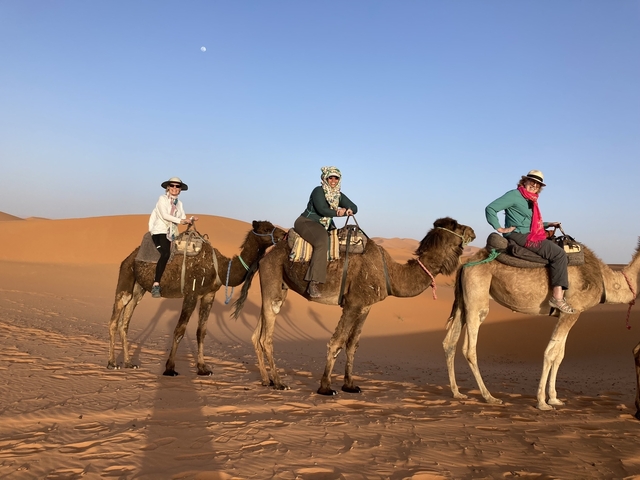       Three people riding camels through a desert.
  
