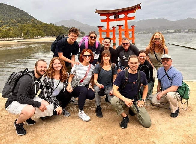 Group of people posing in front of the Itsukushima Shrine gate.
