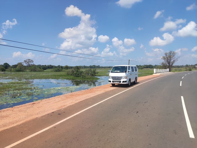       White van parked by the roadside near a water body.
  