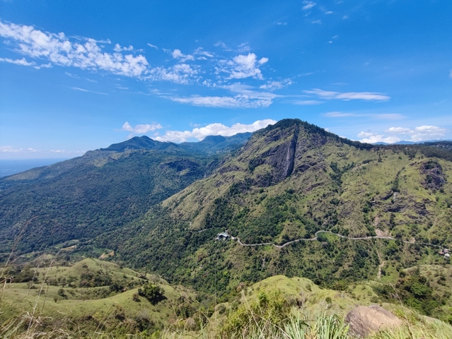       Green hills and mountains under a blue sky.
  